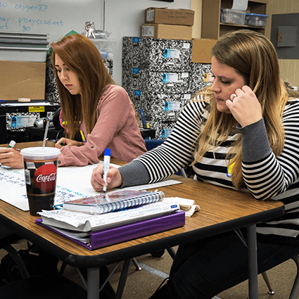 Two female students working together on mini white board at desk