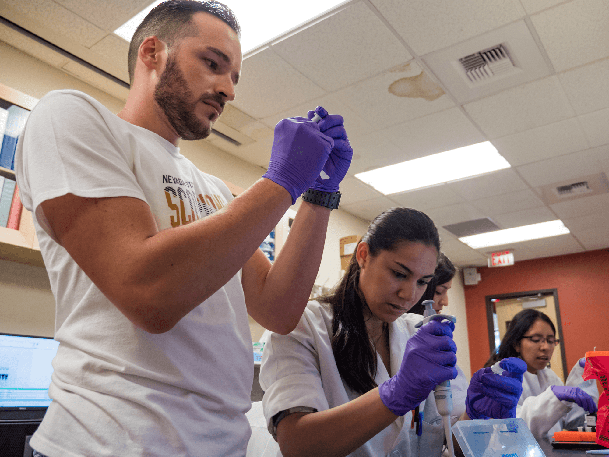 Four students working together in science lab with gloves on