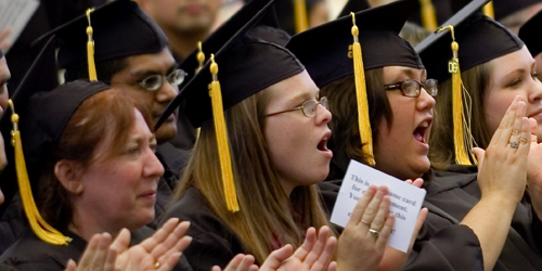 Close up of students in their caps and gowns clapping and cheering at their graduation.