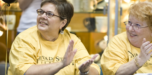 Close up of two women clapping in yellow Nevada State t-shirts.