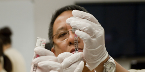 Nursing student extracting a liquid from a vile with a syringe.