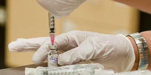 Close up of a person wearing gloves contracting a liquid from a vile with a syringe.