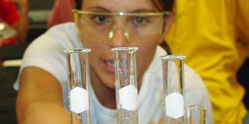 Woman with googles on looking at different sized test tubes