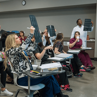 Picture of students in classroom; some students holding up x-rays in light to look at them closer