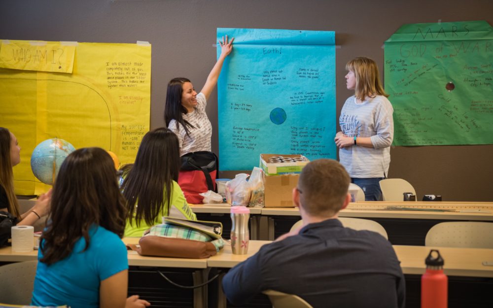 Picture of education classroom at Nevada State College where two female students are presenting with a large piece of butcher paper