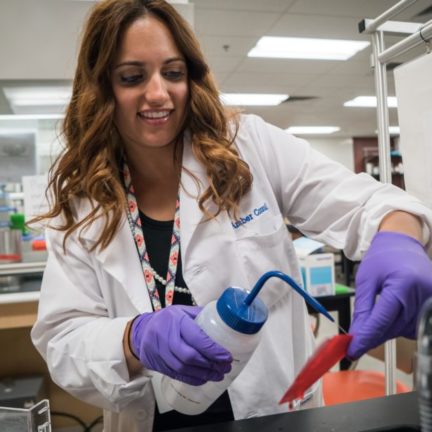 Student working in a lab with a white coat on using distilled water