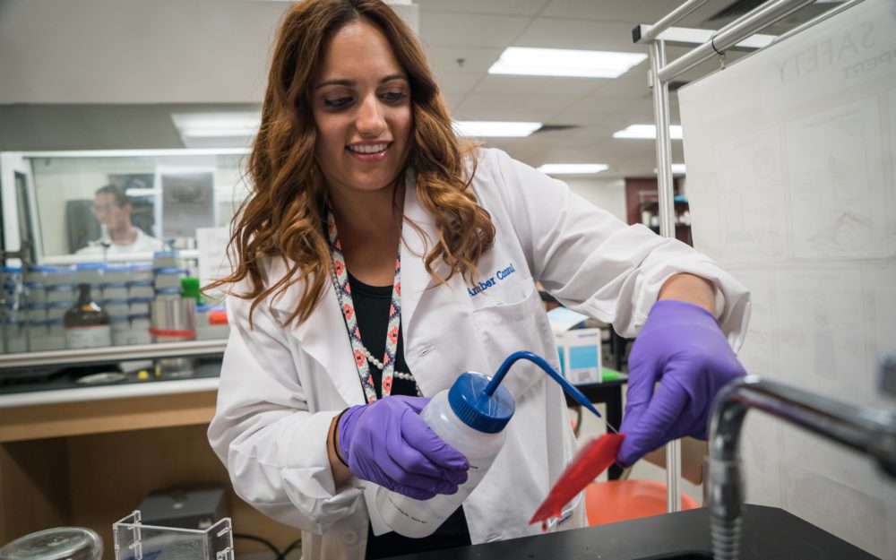 Student working in a lab with a white coat on using distilled water