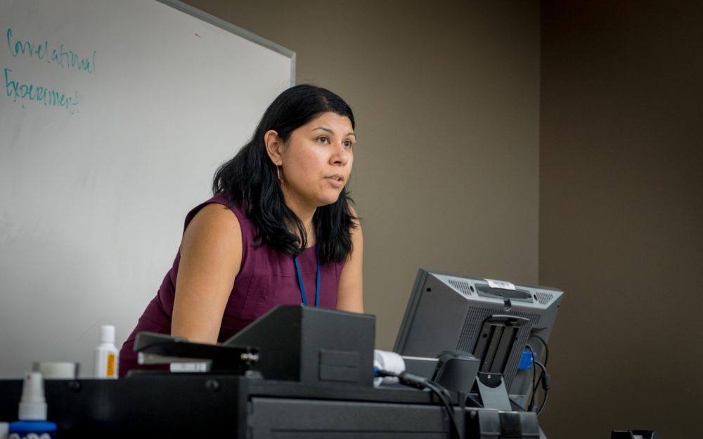 Picture of Psychology Professor, Dr. Laura Naumann at the front of the classroom behind a computer