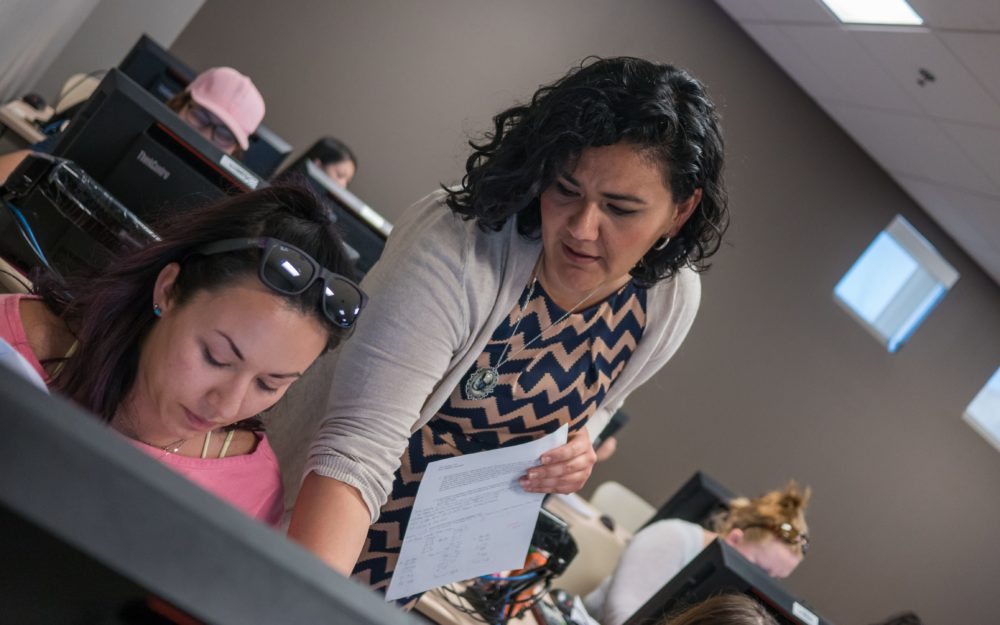 Professor leaning over student shoulder to help her on the computer