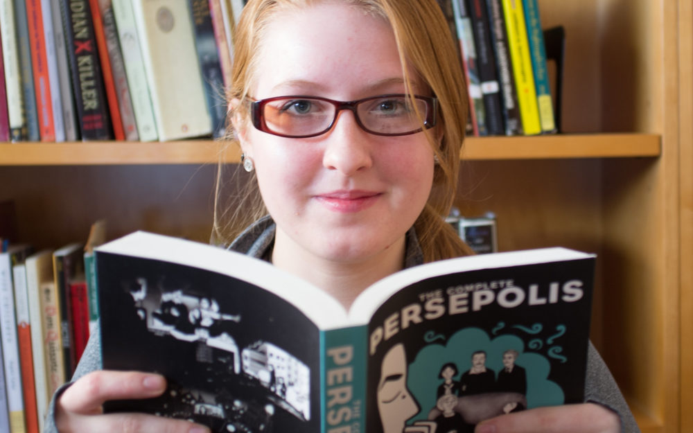 Student reading book, Persepolis while looking at camera