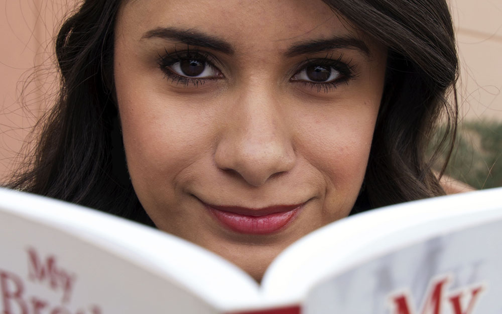 Student reading a book while looking and smiling at camera