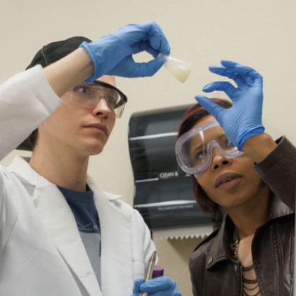 Two students in chemistry lab looking at liquid in bottle