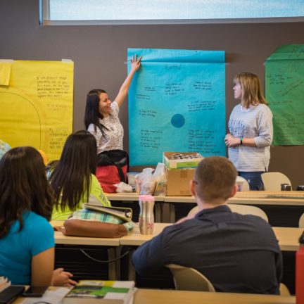 Two students presenting in front of class with poster on wall