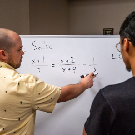 Student writing out equation on white board for other student